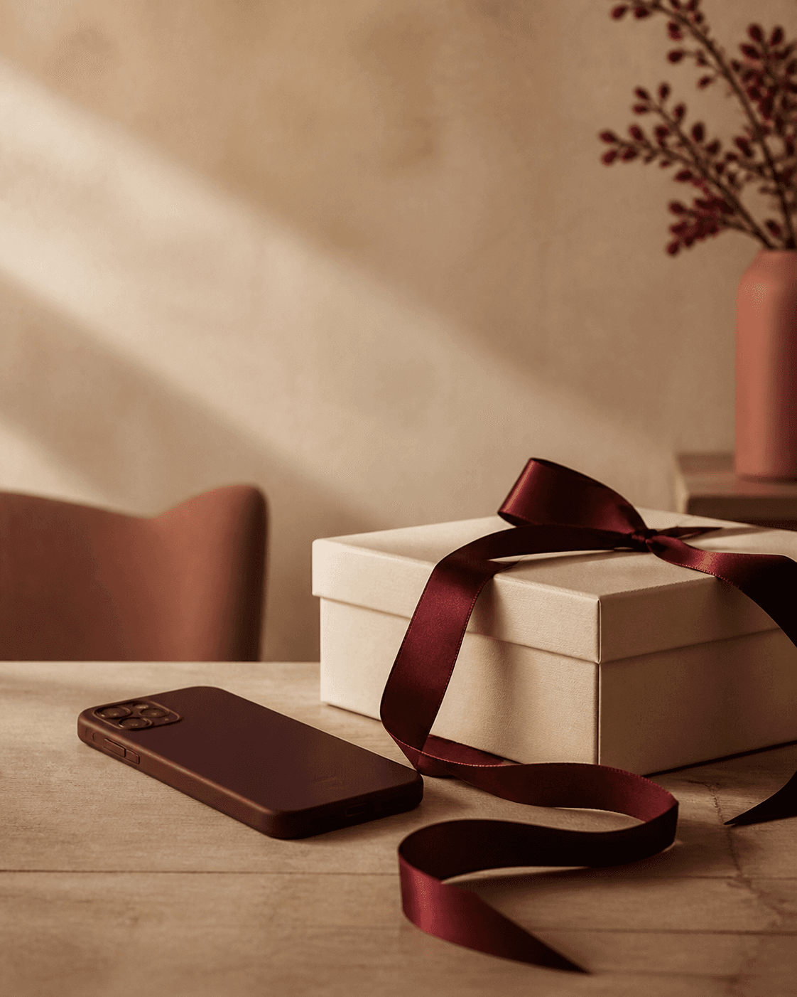 Teléfono boca abajo junto a una caja de regalo cerrada con un lazo color vino.
